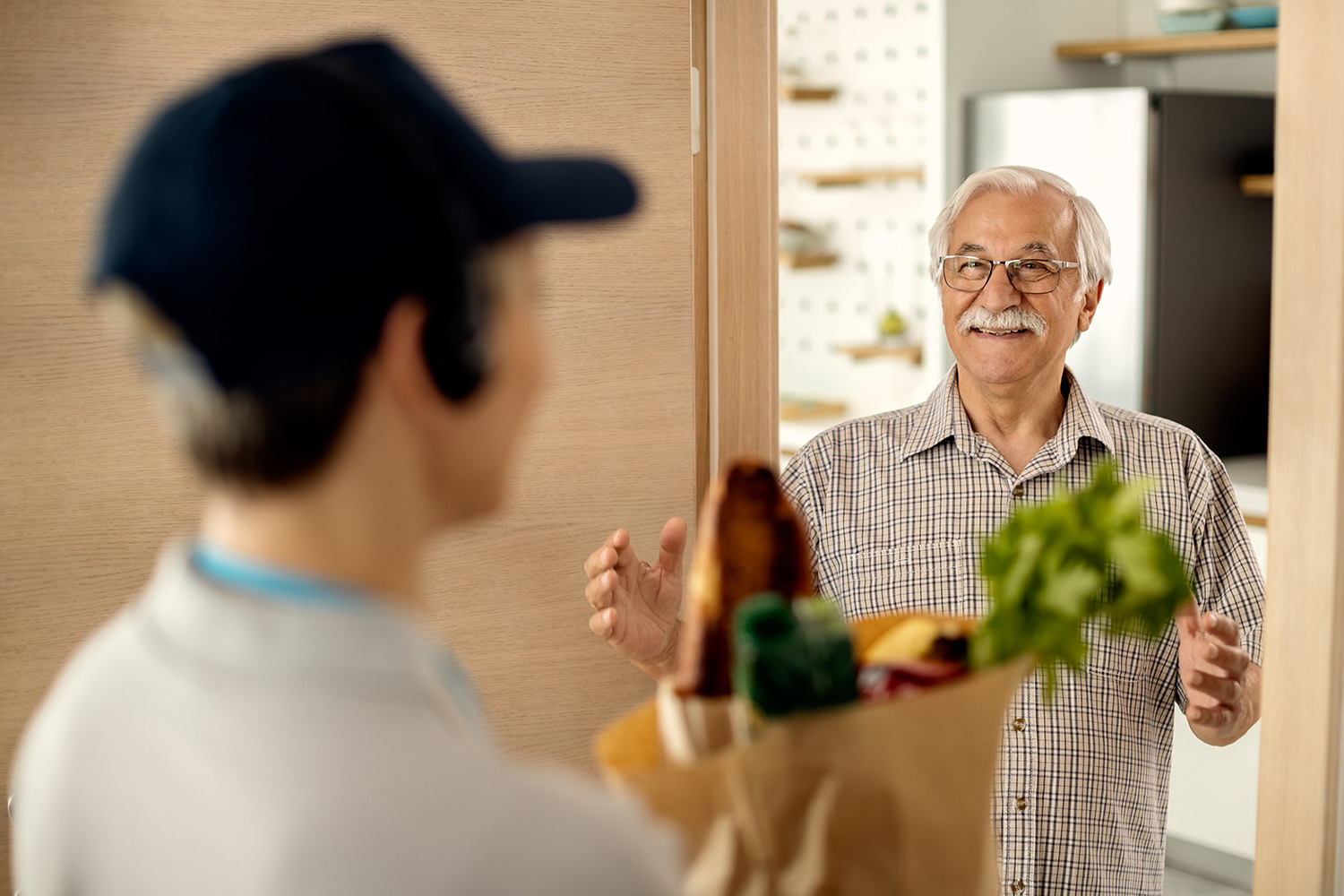 Ein Lieferant übergibt einem senior Herrn eine Einkaufslieferung an der Haustür